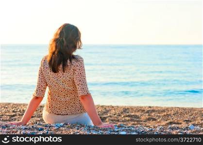 woman admiring the sea while sitting on a pebble beach