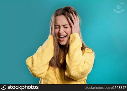 Woman afraid of something, she in shock on blue backdrop.Holding head, screaming. High quality photo. Woman afraid of something, she in shock on blue backdrop.Holding head, screaming