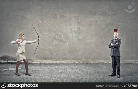 Woman aiming her goal. Young woman archer in suit aiming to shoot apple on man head