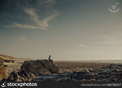Woman alone in the beach sitting on the rocks