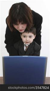 Woman and boy in suits at desk with laptop.