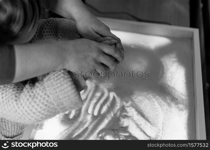 Woman and child draw with their fingers on an interactive sand table. Shallow depth of field.