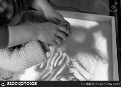 Woman and child draw with their fingers on an interactive sand table. Shallow depth of field.