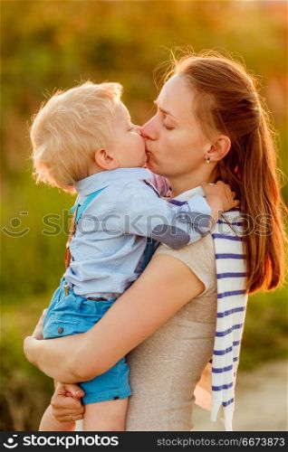 Woman and child outdoors at sunset. Boy kissing his mom.. Happy woman and child having fun outdoors. Family lifestyle rural scene of mother and son in sunset sunlight. Boy kissing his mom.
