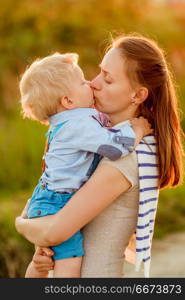 Woman and child outdoors at sunset. Boy kissing his mom.. Happy woman and child having fun outdoors. Family lifestyle rural scene of mother and son in sunset sunlight. Boy kissing his mom.