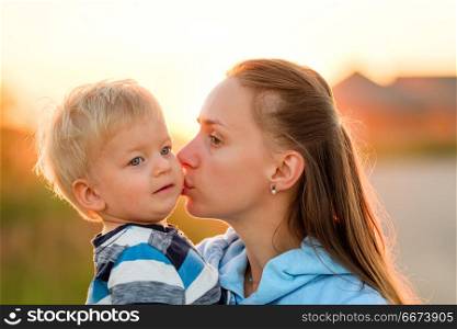 Woman and child outdoors at sunset. Mother kissing her son. . Happy woman and child having fun outdoors. Family lifestyle rural scene of mother and son in sunset sunlight. Mother kissing her son.