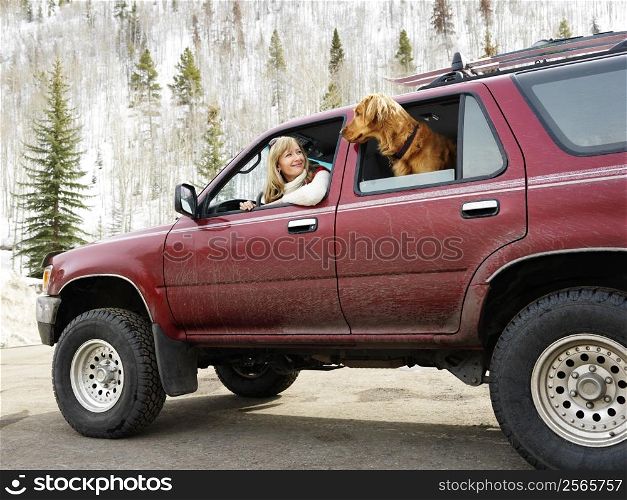 Woman and dog in dirt splattered SUV looking out windows at eachother in snowy countryside.