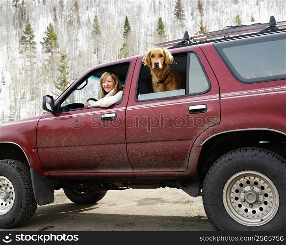 Woman and dog in dirt splattered SUV looking out windows in snowy countryside.
