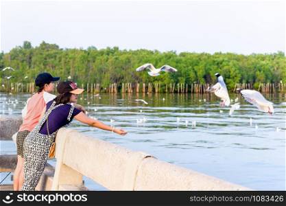 Woman and girl Asian family tourist, mother and daughter are happy fun feeding the seagulls flying above the sea, Travel Asia at Bangpu Recreation Center, Famous attraction of Samut Prakan, Thailand. Mother and daughter enjoy feeding the seagull