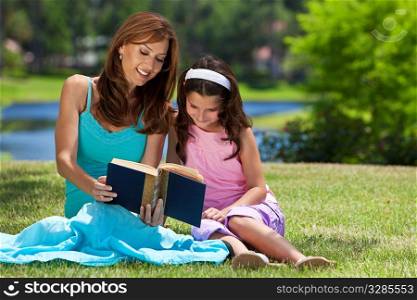 Woman and girl, mother and daughter, reading a book together outside in the countryside