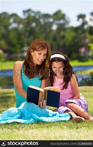 Woman and girl, mother and daughter, reading a book together outside in the countryside