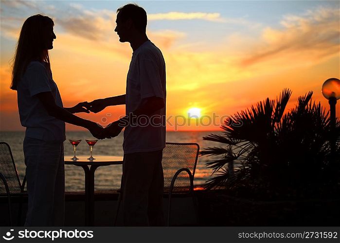 woman and man keep for hands against sunset on sea