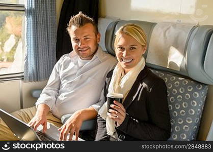 Woman and man sitting in train smiling laptop coffee commuters