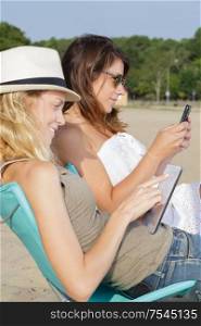 woman and sister using tablet and phone at the sea