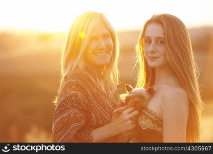Woman and teenager standing in field at dusk holding domestic dog