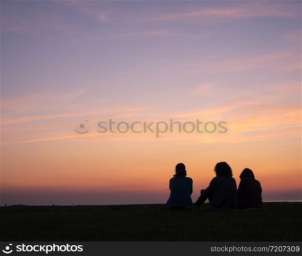woman and two children sit together watching colorful sunset
