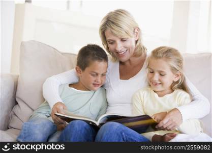 Woman and two children sitting in living room reading book and smiling