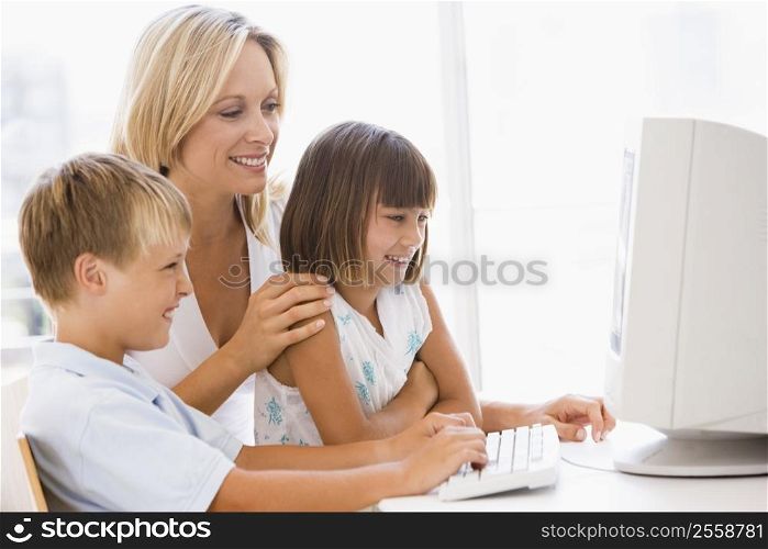 Woman and two young children in home office with computer smiling