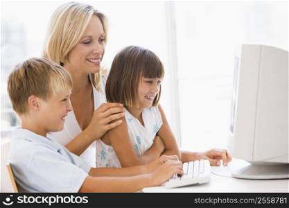 Woman and two young children in home office with computer smiling