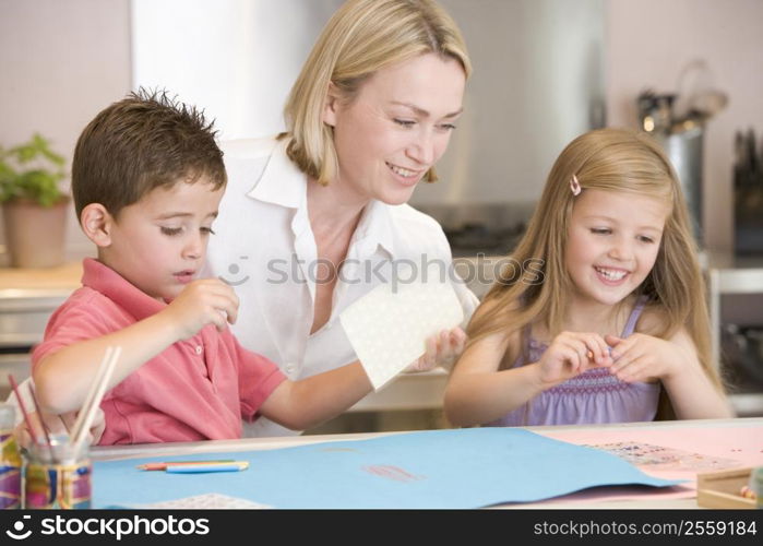 Woman and two young children in kitchen with art project smiling