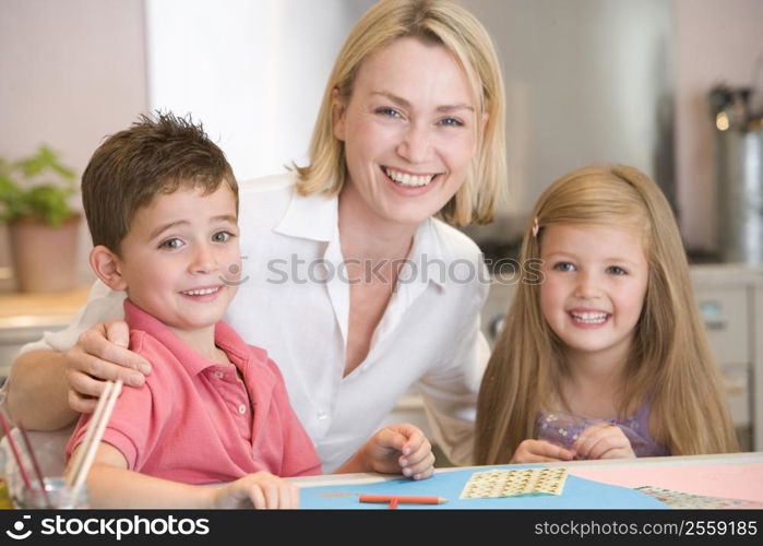 Woman and two young children in kitchen with art project smiling