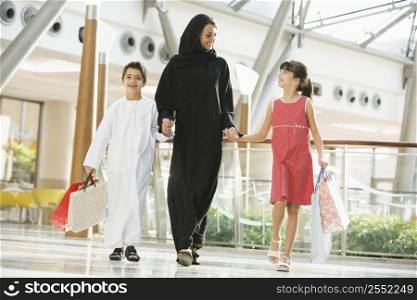 Woman and two young children walking in mall holding hands and smiling (selective focus)