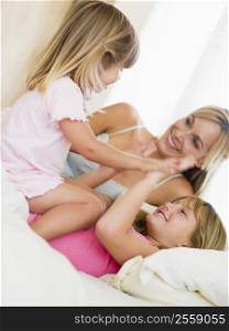 Woman and two young girls in bed playing and smiling