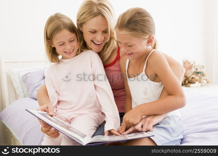 Woman and two young girls in bedroom reading book and smiling
