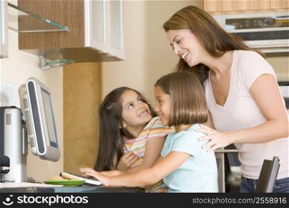 Woman and two young girls in kitchen with computer smiling