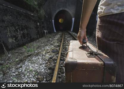 Woman and vintage suitcase on railway road and tunnel.
