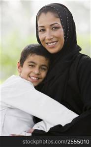 Woman and young boy outdoors in park embracing and smiling (selective focus)