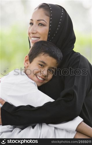 Woman and young boy outdoors in park embracing and smiling (selective focus)