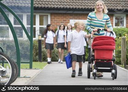 Woman and young boy pushing a stroller outside school with students in background (selective focus)