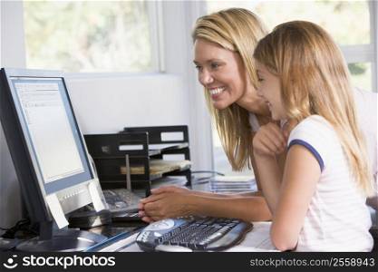 Woman and young girl in home office with computer smiling