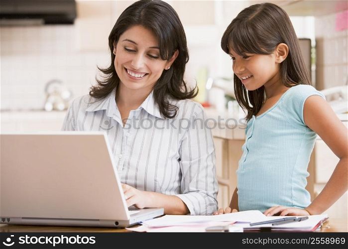 Woman and young girl in kitchen with laptop and paperwork smiling
