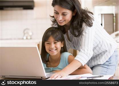 Woman and young girl in kitchen with laptop and paperwork smiling