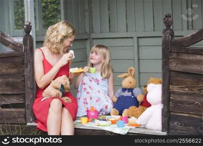 Woman and young girl in shed playing tea and smiling