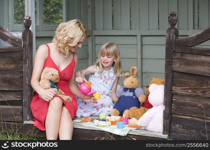 Woman and young girl in shed playing tea and smiling