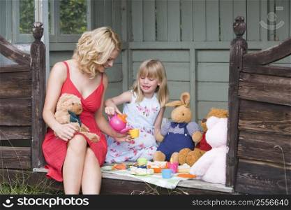 Woman and young girl in shed playing tea and smiling