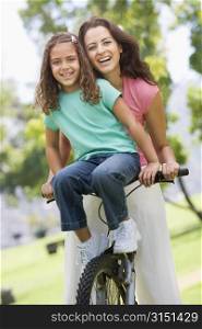 Woman and young girl on a bike outdoors smiling