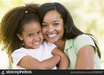 Woman and young girl outdoors embracing and smiling