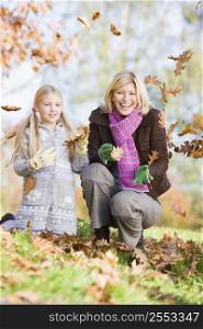 Woman and young girl outdoors in park playing in leaves and smiling (selective focus)