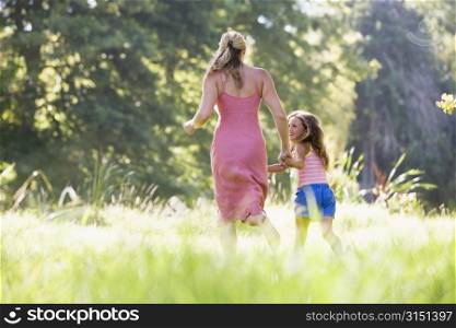 Woman and young girl running outdoors holding hands and smiling