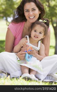 Woman and young girl sitting outdoors with toy smiling