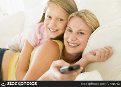 Woman and young girl with remote control embracing on sofa smiling