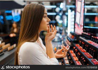 Woman applies lipstick in cosmetics store. Buyer at the showcase in luxury beauty shop salon, female customer in fashion market. Woman applies lipstick in cosmetics store