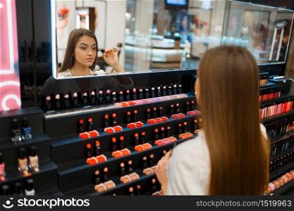 Woman applies mascara at the mirror in cosmetics store. Buyer at the showcase in luxury beauty shop salon, female customer in fashion market. Woman applies mascara in cosmetics store