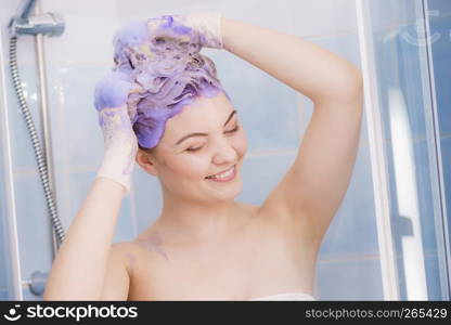 Woman applying coloring shampoo on her hair. Female having purple washing product. Toning blonde color at home.. Woman applying toner shampoo on her hair