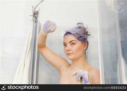 Woman applying coloring shampoo on her hair. Female having purple washing product. Toning blonde color at home.. Woman applying toner shampoo on her hair