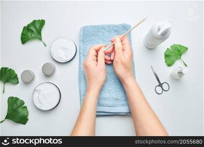 Woman applying cosmetic moisturizing hand cream. Cosmetic products, green leaves on white table. Spa, manicure, skin care concept. Flat lay, overhead view